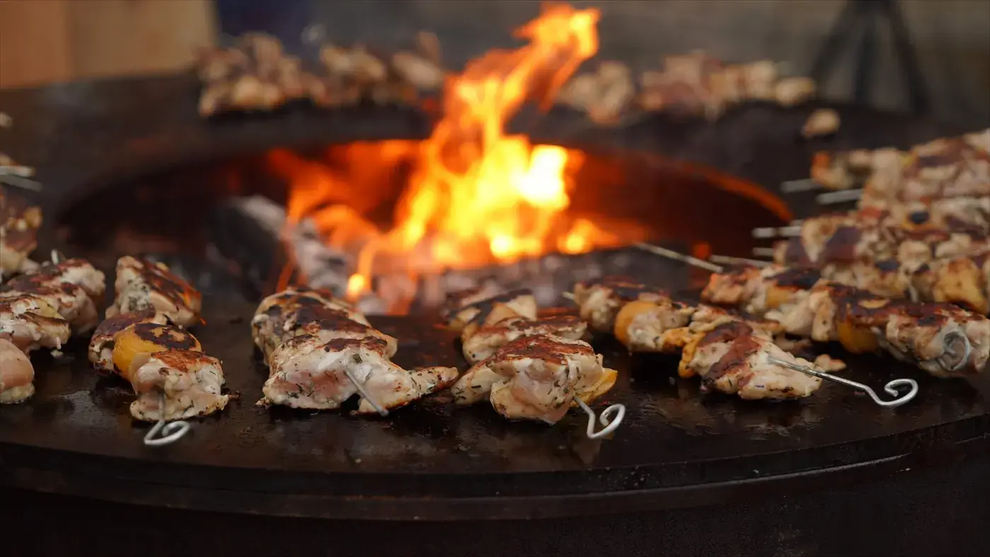 Des brochettes qui cuisent sur le brasero, flammes au centre.