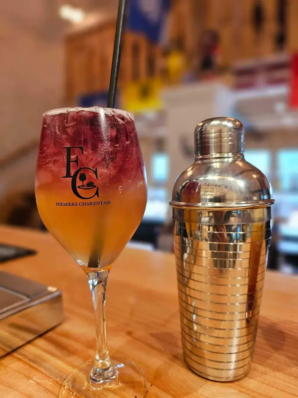 Un verre à pied au logo des Fermiers Charentais, à côté du shaker.