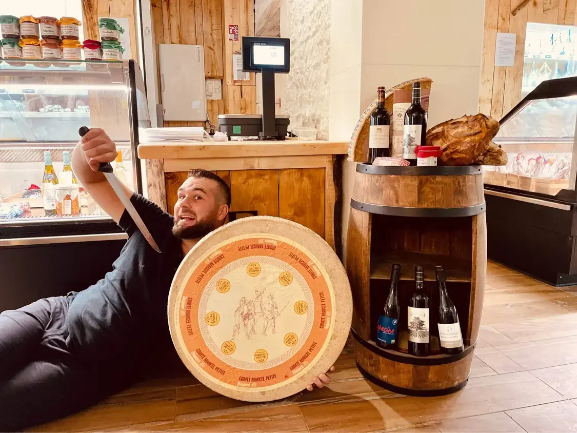 Un membre de l’équipe allongé par terre dans le magasin, une meule de comté dans les bras.