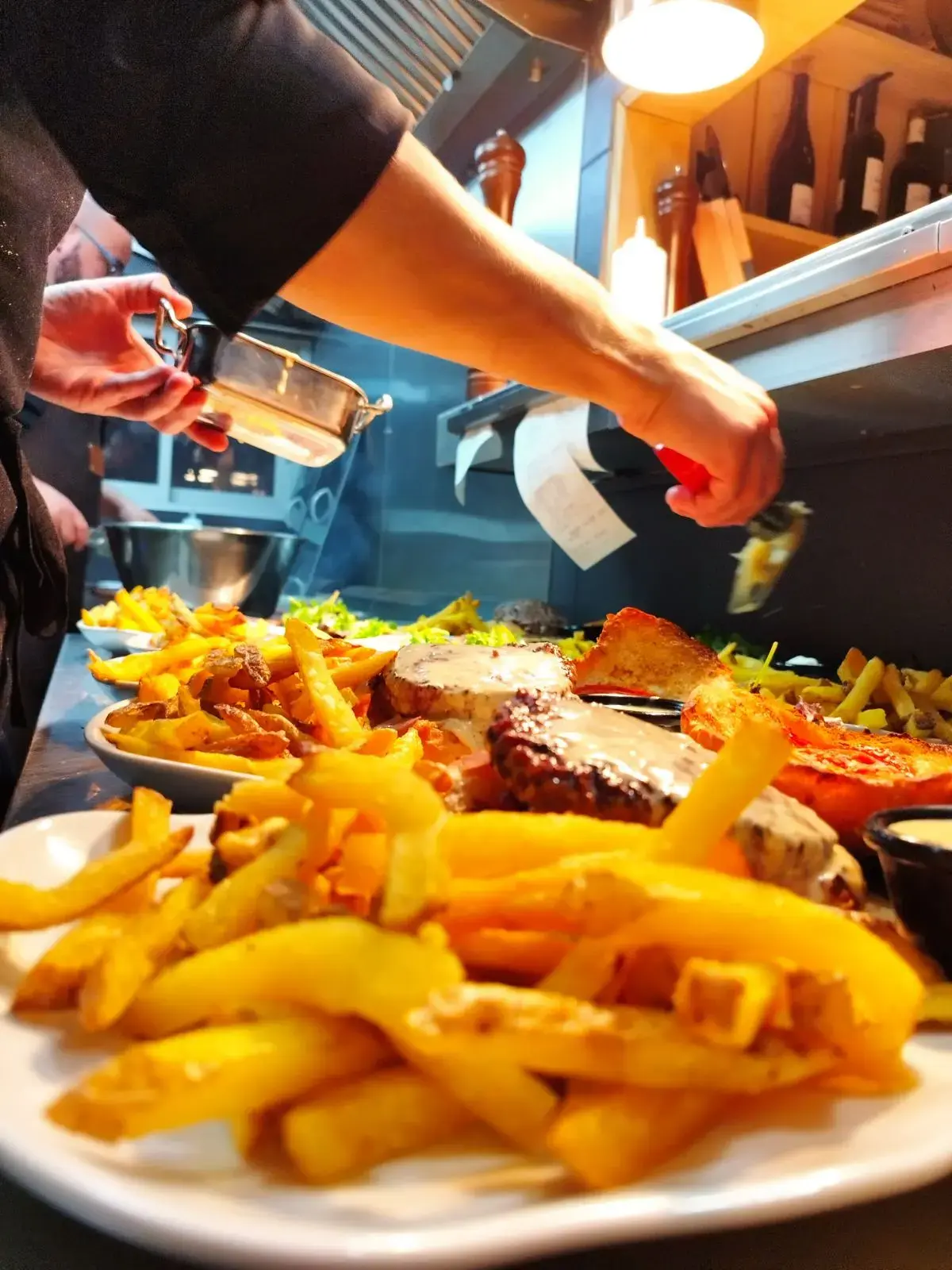 Une assiette en cours de dressage : viande, frites maison et sauce versée dessus.