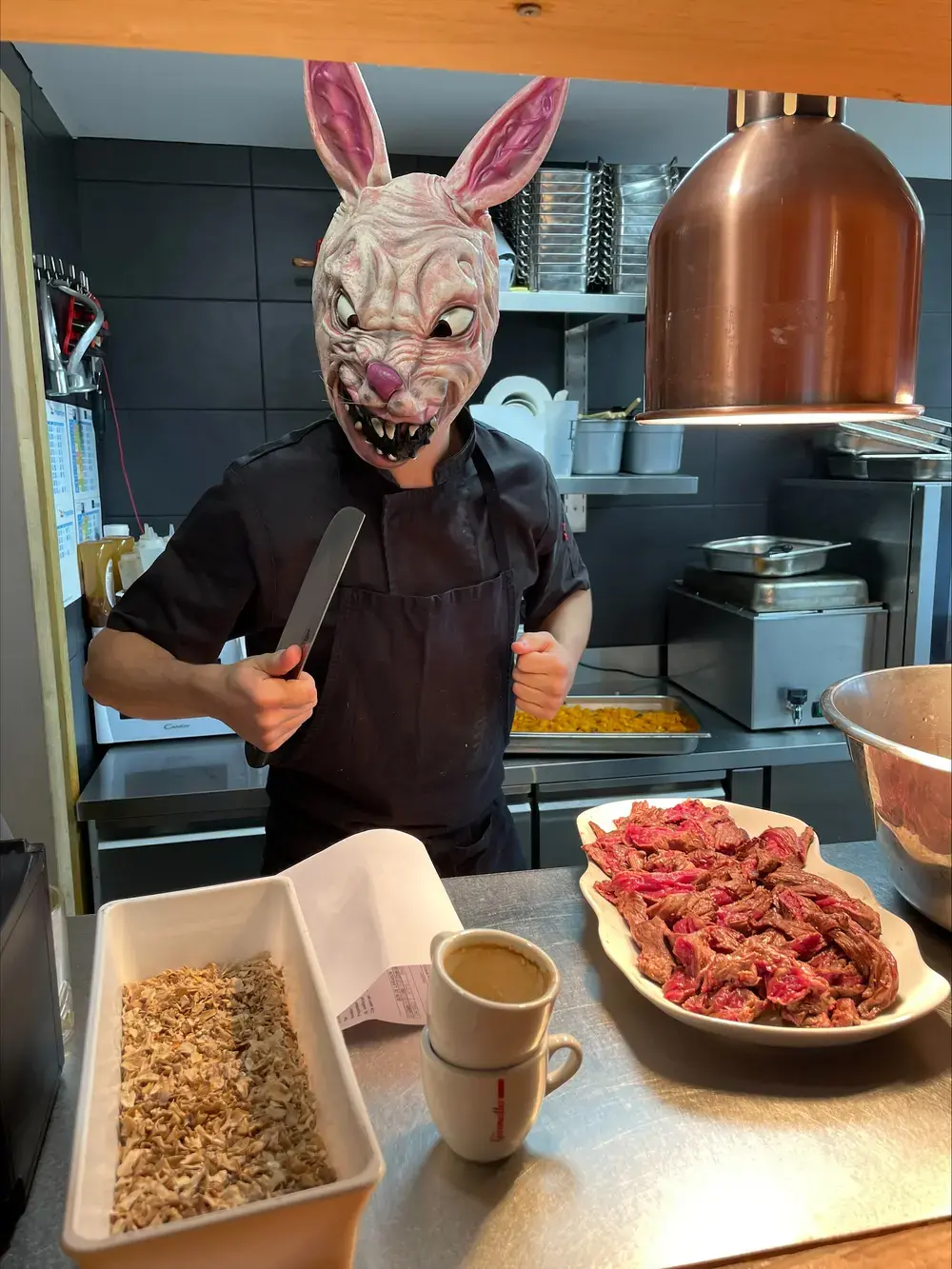 Un cuisinier masqué en lapin, couteau à la main, devant un plat de viande.
