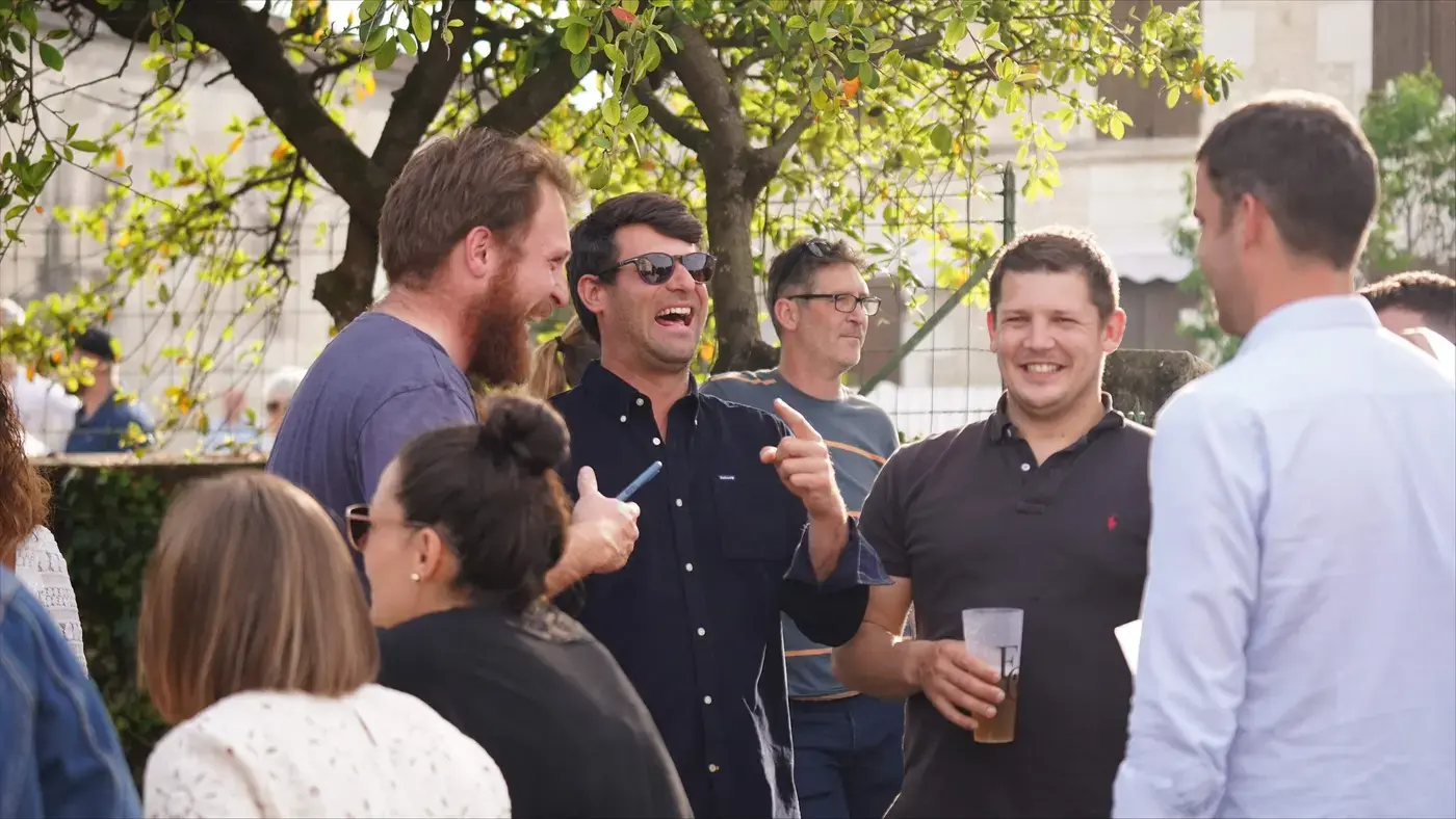 Des clients qui rient, un verre à la main, sous les arbres de la terrasse.