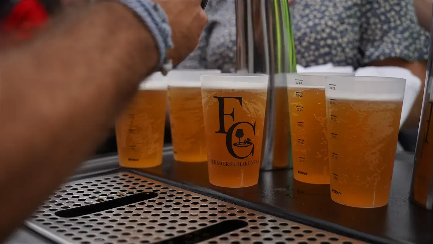 Des gobelets de bière remplis à la tireuse, au logo des Fermiers Charentais.