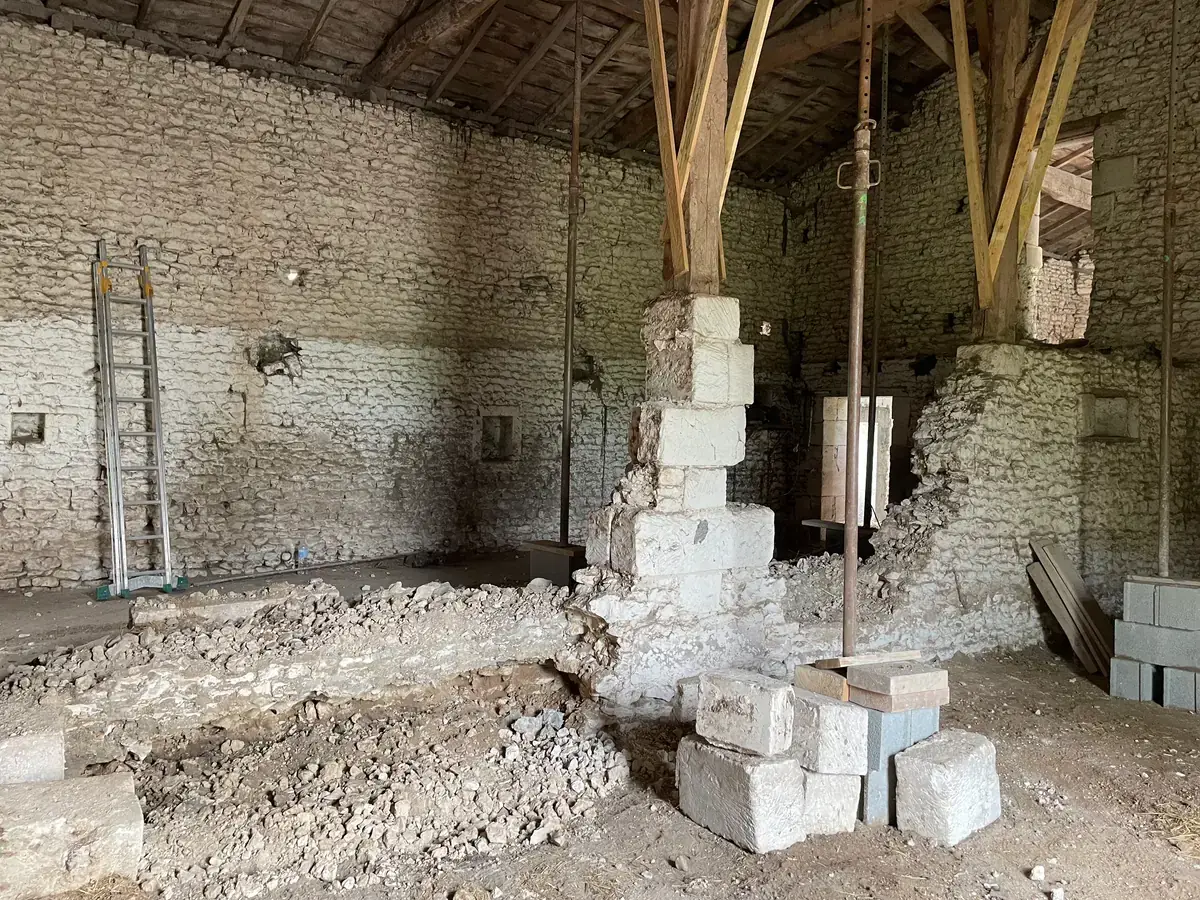 La grange vidée jusqu’à la terre, son pilier de pierre repris en sous-œuvre et la charpente tenue par des étais.