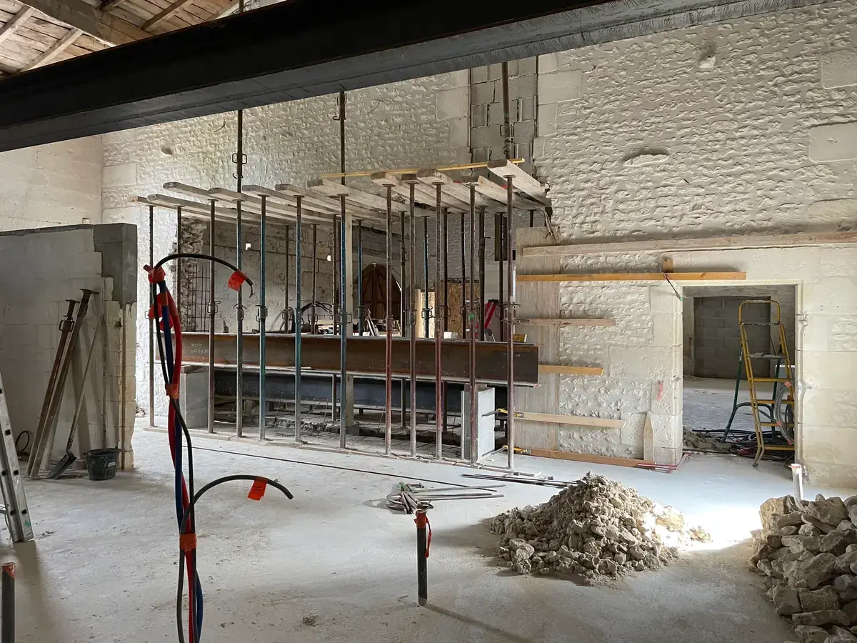 La grande salle en chantier, murs de pierre passés au blanc et poutre d’acier posée en travers de l’ouverture.